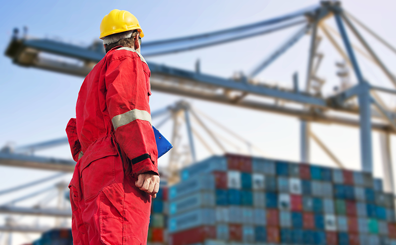 FCL: employee in red overall in port, with many containers and cargo cranes in the background FCL: employee in red overall in port, with many containers and cargo cranes in the background